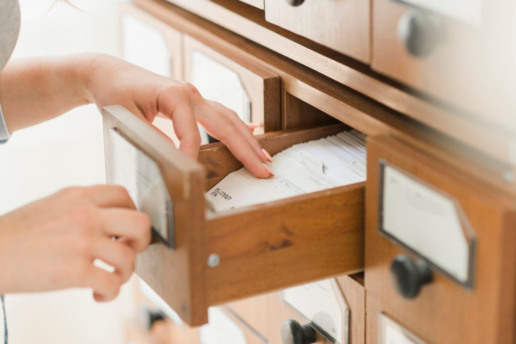 En hand bläddrar bland kort i en utdragen låda i en kortkatalog av trä