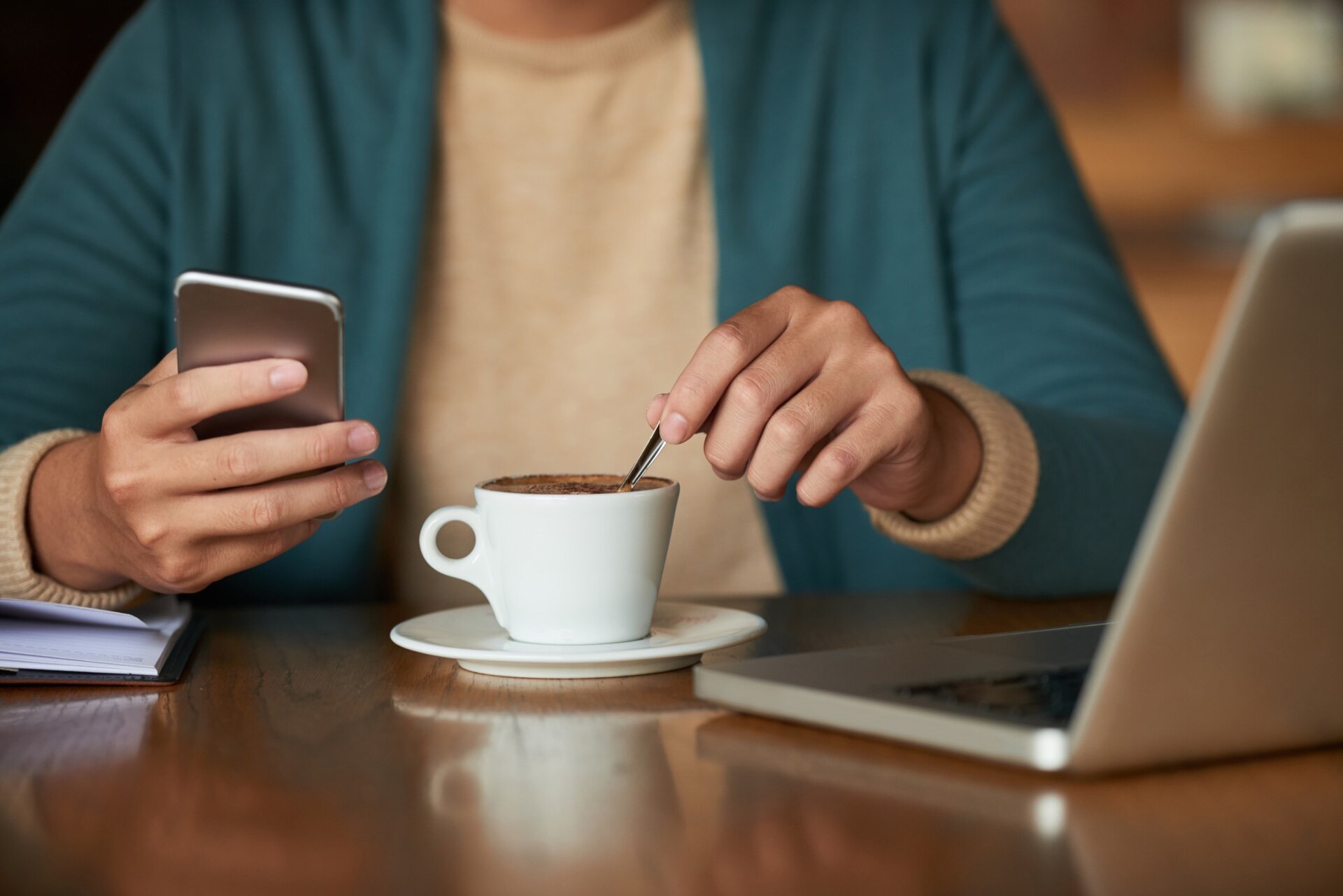 En person läser på sin mobiltelefon och rör om i en kopp kaffe