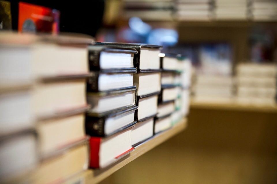Staplade inbundna böcker på en hylla i ett bibliotek med suddig bakgrund